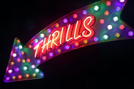 Multi-colored neon signs reading “Thrills” on black background