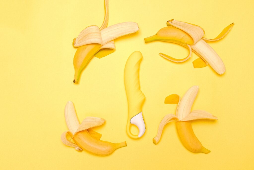 Yellow sex toys surrounded by partially peeled bananas on a yellow background.