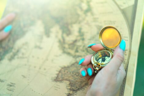 Woman’s hand with blue nails holds compass as she examines old map.