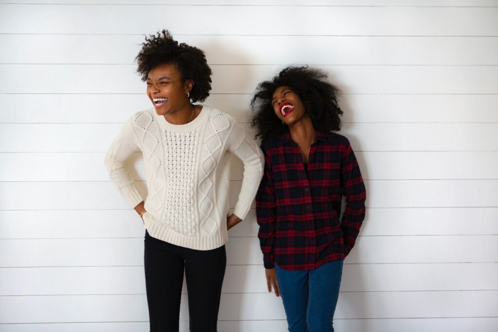 Two women laughing in front of a white, shiplap wall.