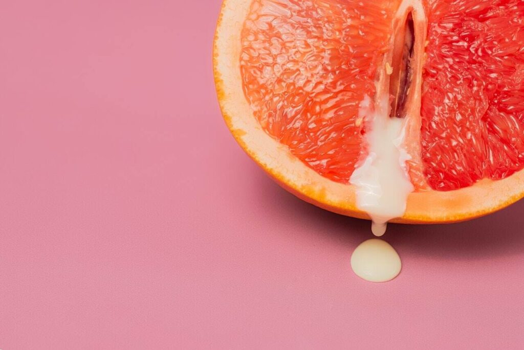 Grapefruit suggestively drips with cream on pink background.