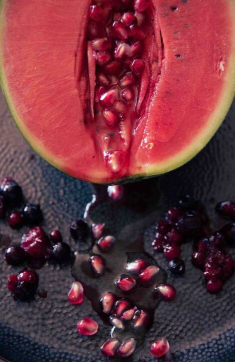 Half watermelon with pomegranate seeds spilling out on black background