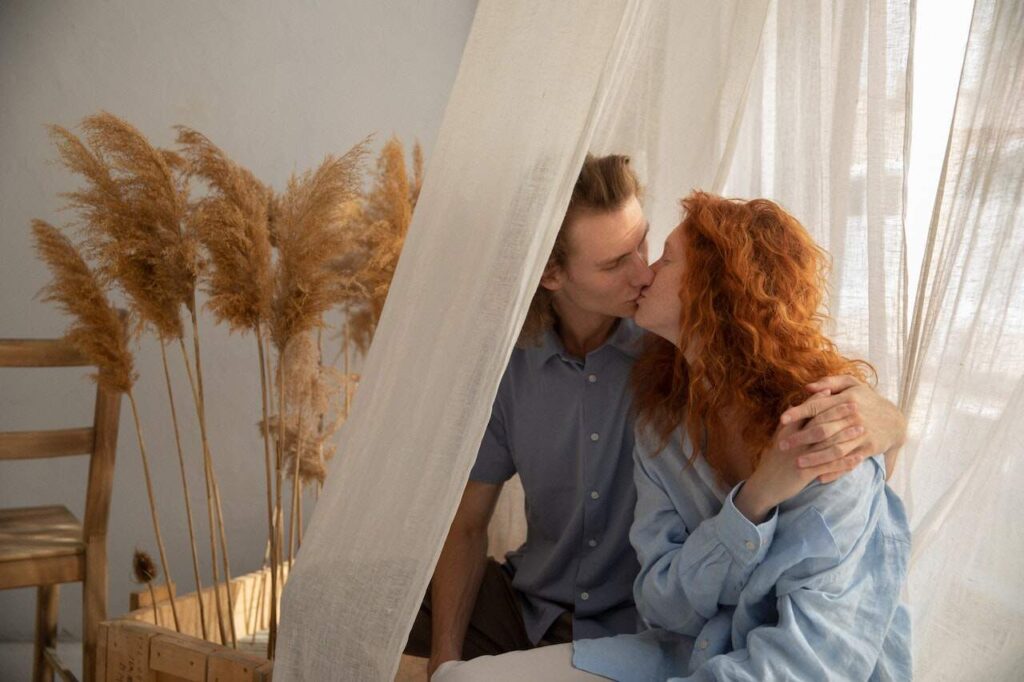 Couple kissing inside mosquito netting over bed, with pampas grass in the background.