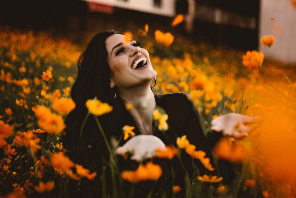 Dark haired woman surrounded by yellow flowers laughs joyfully