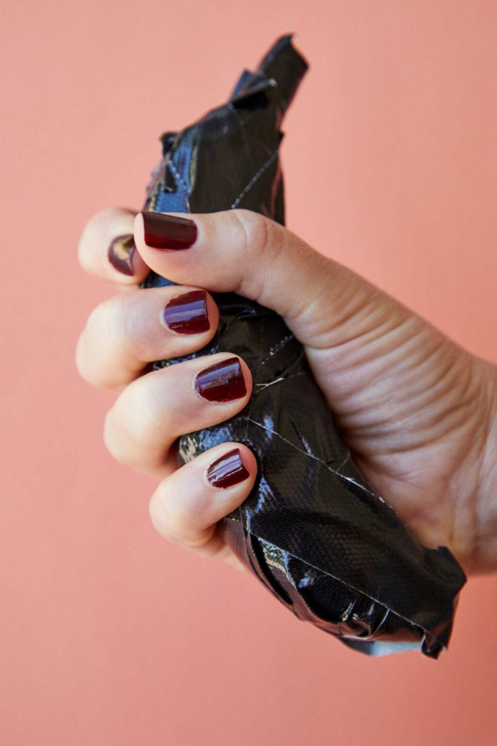 Hand with nails painted deep burgundy holds banana wrap in black duct tape.