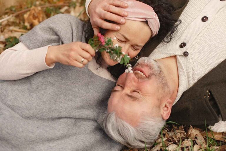 Couple in an intimate moment as woman tickles man with flowers, lying on the ground.