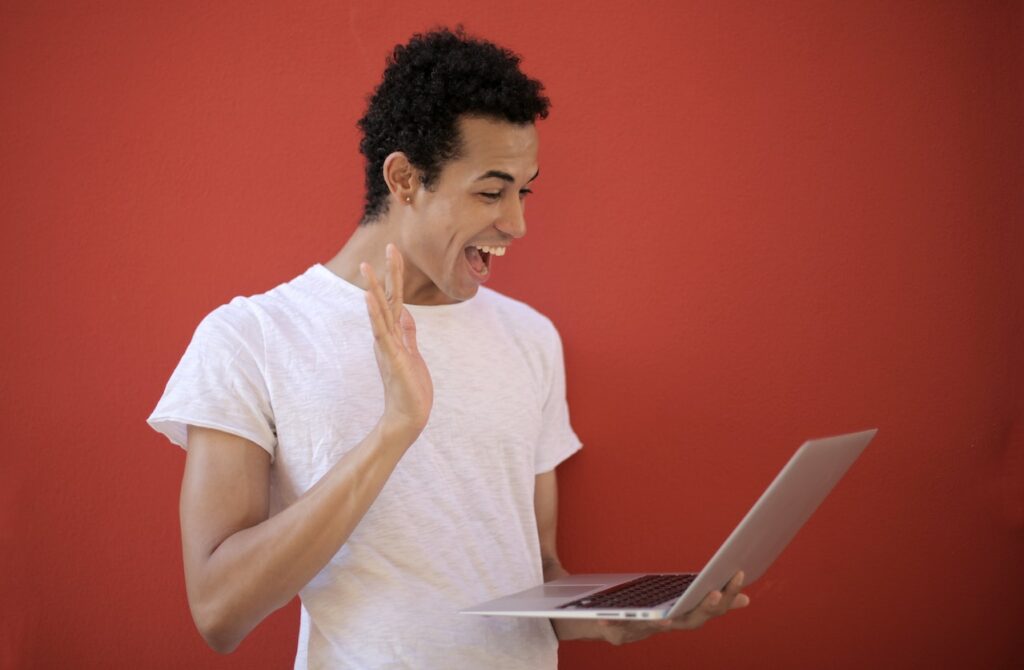 Man with excited expression looking at a laptop against red background.