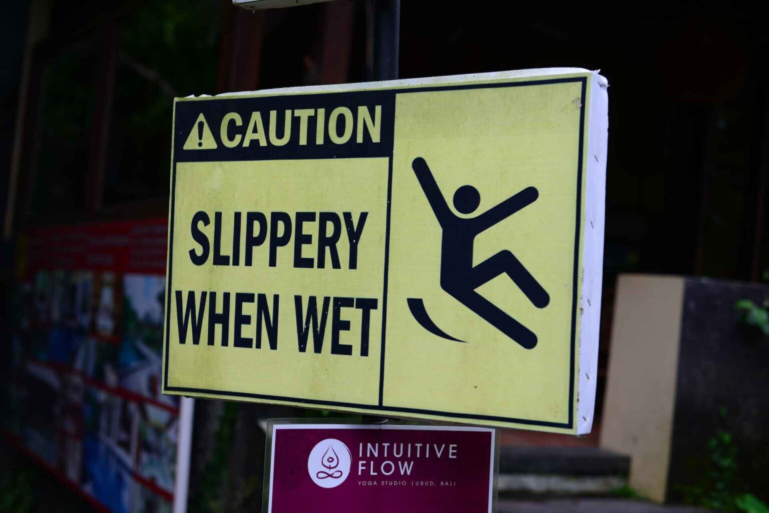 Yellow and black sign cautions “slippery when wet”, with slipping figure.