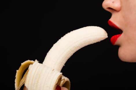 Woman wearing bright red lipstick prepares to bite into a banana.