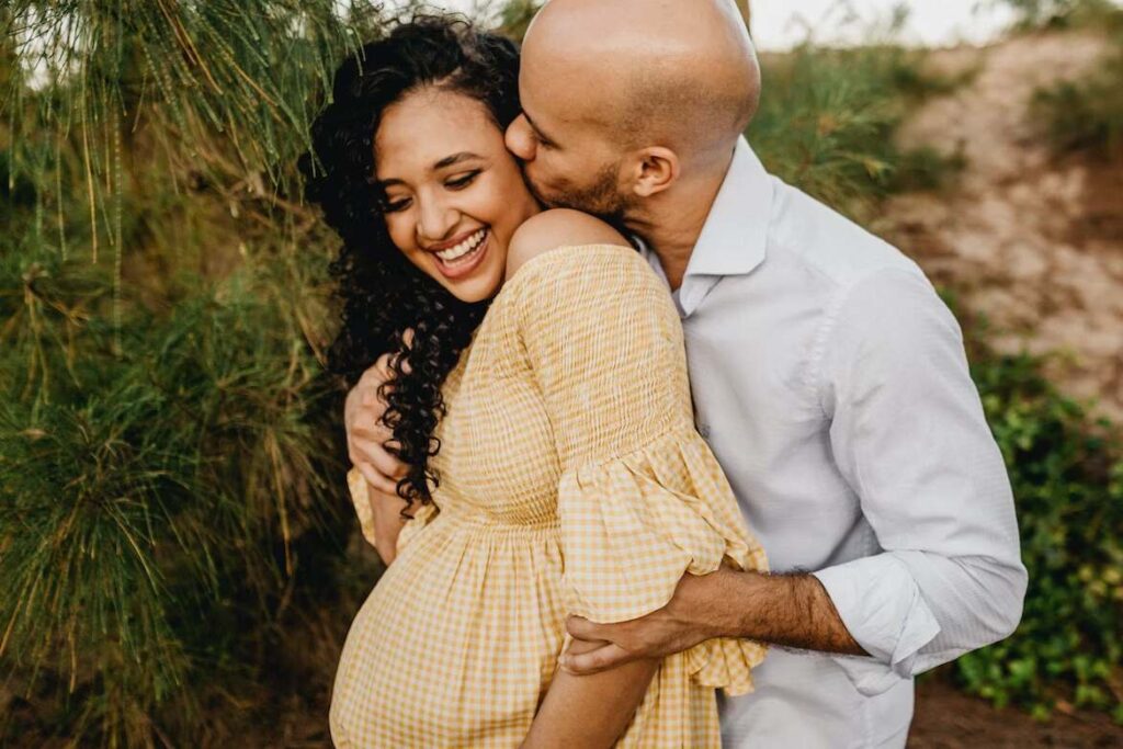 Man kissing pregnant woman from behind.