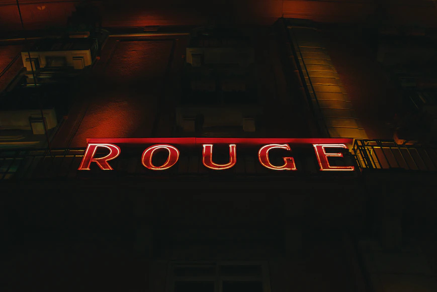 The French word “rouge” (red), spelled out in small caps in red & white neon