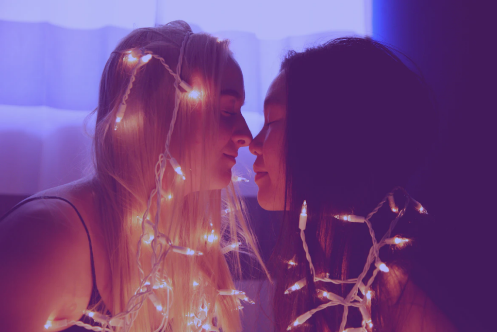 Women draped in fairy lights about to kiss.