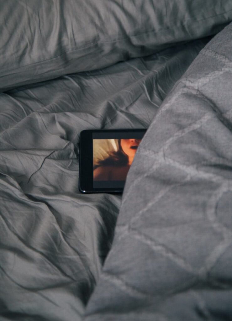 Smartphone partially covered by bed sheets with image of woman in ecstasy